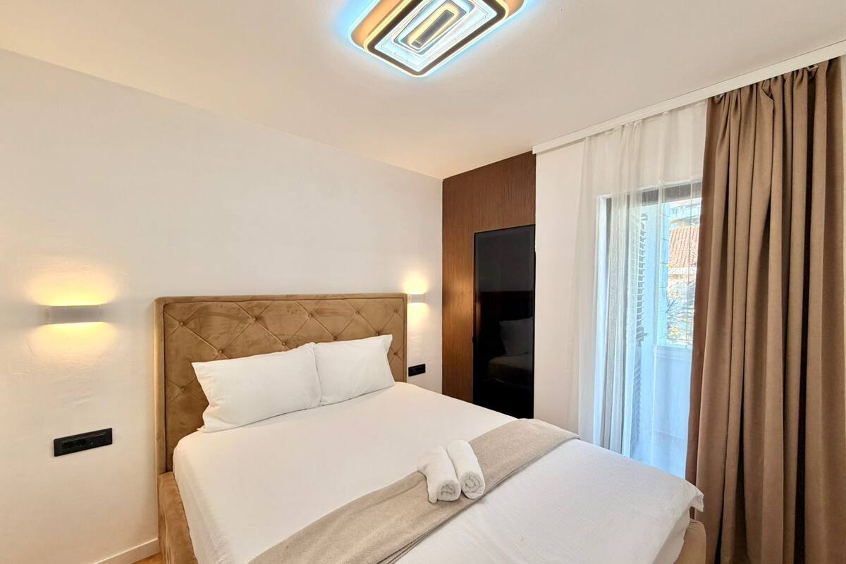 A modern hotel room with a large bed, a wooden headboard, and a view of the city through the window.