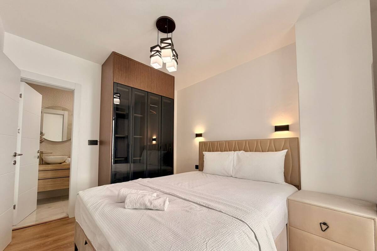 A modern bedroom with a large bed, a wardrobe, a bedside table, and a bathroom visible through an open door.