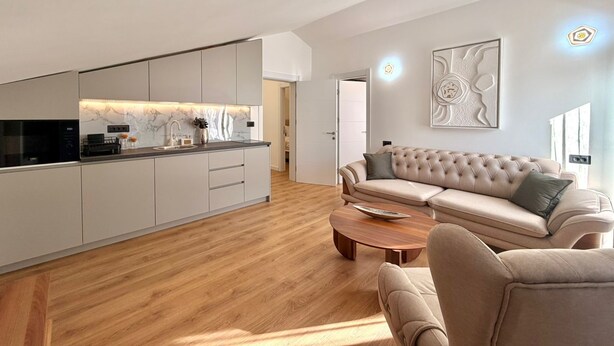 A modern living room with a sofa and coffee table, a kitchen with a marble backsplash, and a large abstract painting on the wall.