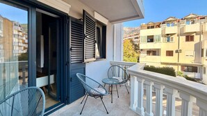 A balcony with two chairs and a table, a sliding glass door, and a view of neighboring buildings.