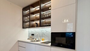 A modern kitchen with white cabinetry, a marble countertop, a built-in oven, and a wine rack above the sink.