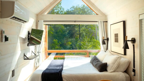 A bedroom with a bed, a TV, a window, and a picture on the wall. - Zen Den Cabin (Houston) (Coldspring)