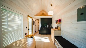 A modern interior with a wooden ceiling, a dining area with a table and chairs, a kitchen with appliances, and a bench. - Zen Den Cabin (Houston) (Coldspring)