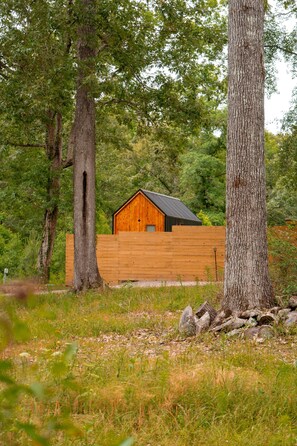 A wooden cabin with a sloped roof, surrounded by trees and a wooden fence. - Zen Den Cabin (Houston) (Coldspring)