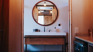 Une salle de bain moderne avec un meuble-lavabo en bois, un miroir rond et un four encastré.