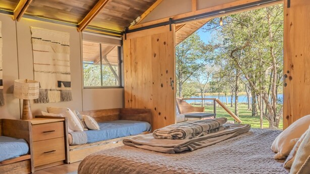 Une chambre dans une cabane en bois, avec un lit, deux petits lits, une table de chevet, une lampe et une vue sur un lac.