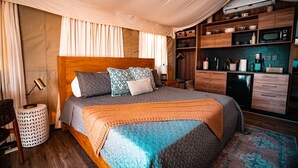 Un dormitorio con cama grande, cabecera de madera, mesitas de noche, armario empotrado y una zona de kitchenette.