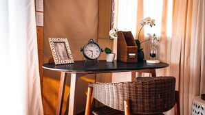 Una pequeña mesa redonda con un marco de madera que contiene una imagen, un reloj analógico negro, una planta en maceta, una caja de madera y un florero de vidrio con flores.