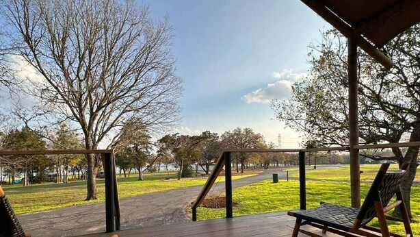 Una terraza de madera con dos sillas de mimbre orientadas hacia un parque cubierto de césped.