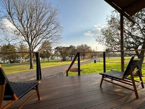 A wooden deck with two wicker chairs facing a grassy park area.