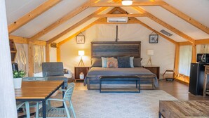 Une chambre confortable avec un grand lit, des poutres apparentes en bois au plafond, une table à manger et un petit coin cuisine.