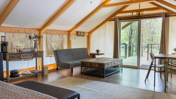 Une pièce chaleureuse et bien éclairée, avec un plafond en bois, un canapé gris, une table basse et un coin repas avec des chaises.