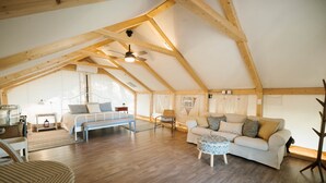 A spacious attic bedroom with a sloped ceiling, wooden beams, a ceiling fan, and a large window allowing natural light. - Lakefront Glamping Safari Tent #5: The Hummingbird (Bastrop County)