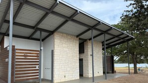 A covered outdoor area with a brick wall, metal beams, and a bench. - Lakefront Glamping Safari Tent #5: The Hummingbird (Bastrop County)