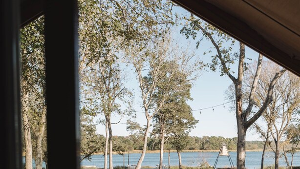 A wooden deck with two red Adirondack chairs facing a lake. - Lakefront Glamping Safari Tent #5: The Hummingbird (Bastrop County)
