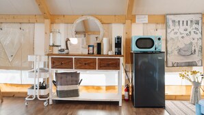 A compact kitchen with a microwave, refrigerator, and a small cart with dishes. - Lakefront Glamping Safari Tent #5: The Hummingbird (Bastrop County)