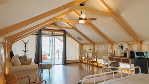 A spacious attic bedroom with a large bed, a wooden ceiling, a dining area, and a view through a large window. - Lakefront Glamping Safari Tent #5: The Hummingbird (Bastrop County)