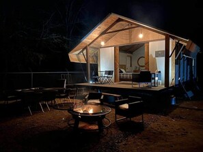 A cozy outdoor seating area with a fire pit, surrounded by chairs and tables, under a covered patio with a view of the interior. - Premium Lakefront Cabin #3: The Firefly (Austin) (Bastrop County)