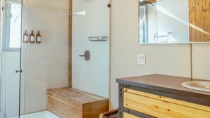Een moderne badkamer met een douchecabine van glas, een houten wastafelmeubel en een spiegel met houten lijst.