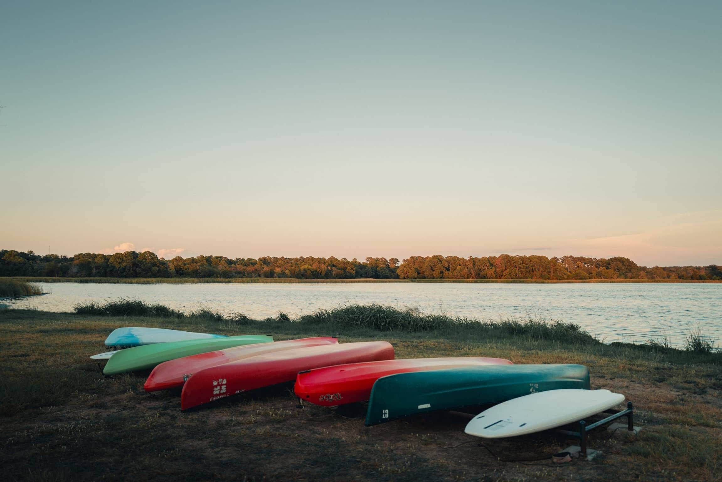 A row of colorful kayaks lined up on a grassy lakeside.