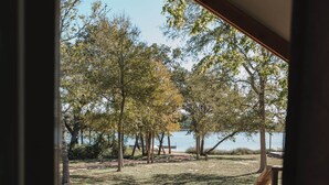 Eine Holzdielen-Terrasse mit roten Adirondack-Stühlen und einem Tisch, mit Blick auf eine grüne Wiese mit Bäumen und einem Gewässer.