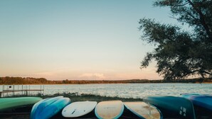Diverse tavole da wakeboard allineate su un'area erbosa vicino a un lago, con un pontile sullo sfondo.