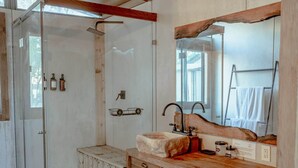 Un bagno con cabina doccia in vetro, mobile lavabo in legno e un ampio specchio con cornice in legno rustico.