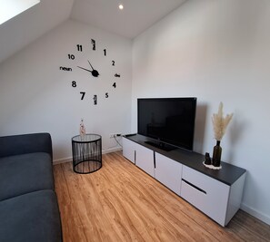 A modern living room with a large wall clock, a flat-screen TV, a sofa, a coffee table, and a cabinet with decorative items.