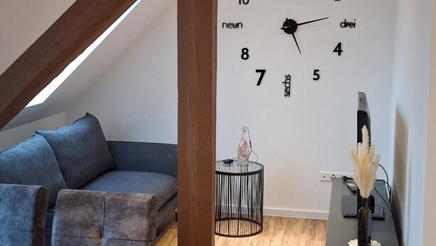 Ein modernes Loft mit einem Holzesstisch, einem grauen Sofa und einer Wanduhr.