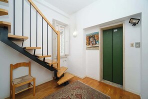 Una escala amb graons de fusta i baranes negres, una porta d'ascensor verd, una cadira i una catifa amb dibuixos.