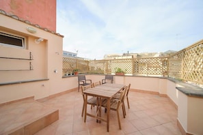 Un patio con una mesa y sillas de madera, piso de baldosas y un cerramiento de celosía.