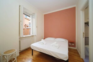 Ein Schlafzimmer mit Bett, Fenster, Heizkörper und einem kleinen Tisch.