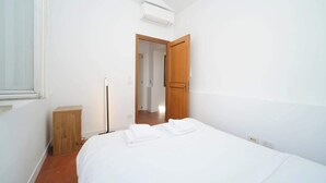Un dormitorio con cama, una puerta de madera, una mesita de noche y un equipo de aire acondicionado.