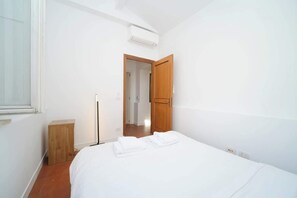 A bedroom with a bed, a wooden door, a bedside table, and an air conditioning unit. - BuddyRent - Duplex terrazza - Trevi - 12 ospiti (roma)