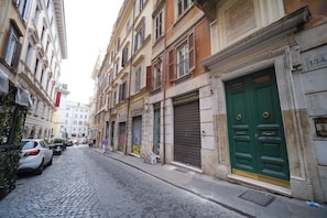 Una calle adoquinada con coches estacionados, comercios cerrados y una puerta verde a la derecha.