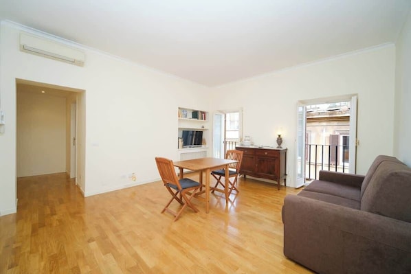 Amplia sala de estar con mesa y sillas de madera, un sofá y una zona de cocina con armarios y una ventana.