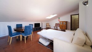Una habitación compacta con cama, sofá, mesa de comedor con sillas, televisor y un mueble.