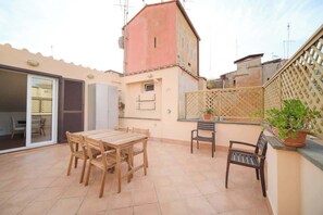 Un patio con mesa y sillas de madera, una planta en maceta y vista a un edificio con techo rojo.
