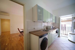 Una cuina compacta amb rentadora, una zona de menjador amb una cadira, i vista exterior.