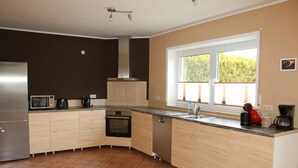 Een moderne keuken met een inbouwoven, magnetron en vaatwasser, een groot raam met uitzicht op groen, en een roestvrijstalen koelkast.