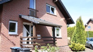 Een huis van baksteen met twee verdiepingen, een balkon, een houten hek en een kleine tuin.