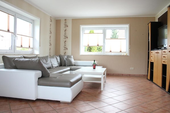 A modern living room with a sectional sofa, a coffee table, a TV, and a window with blinds.