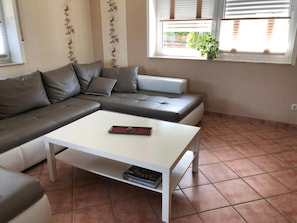 A modern living room with a sectional sofa, a white coffee table, and a window with blinds.