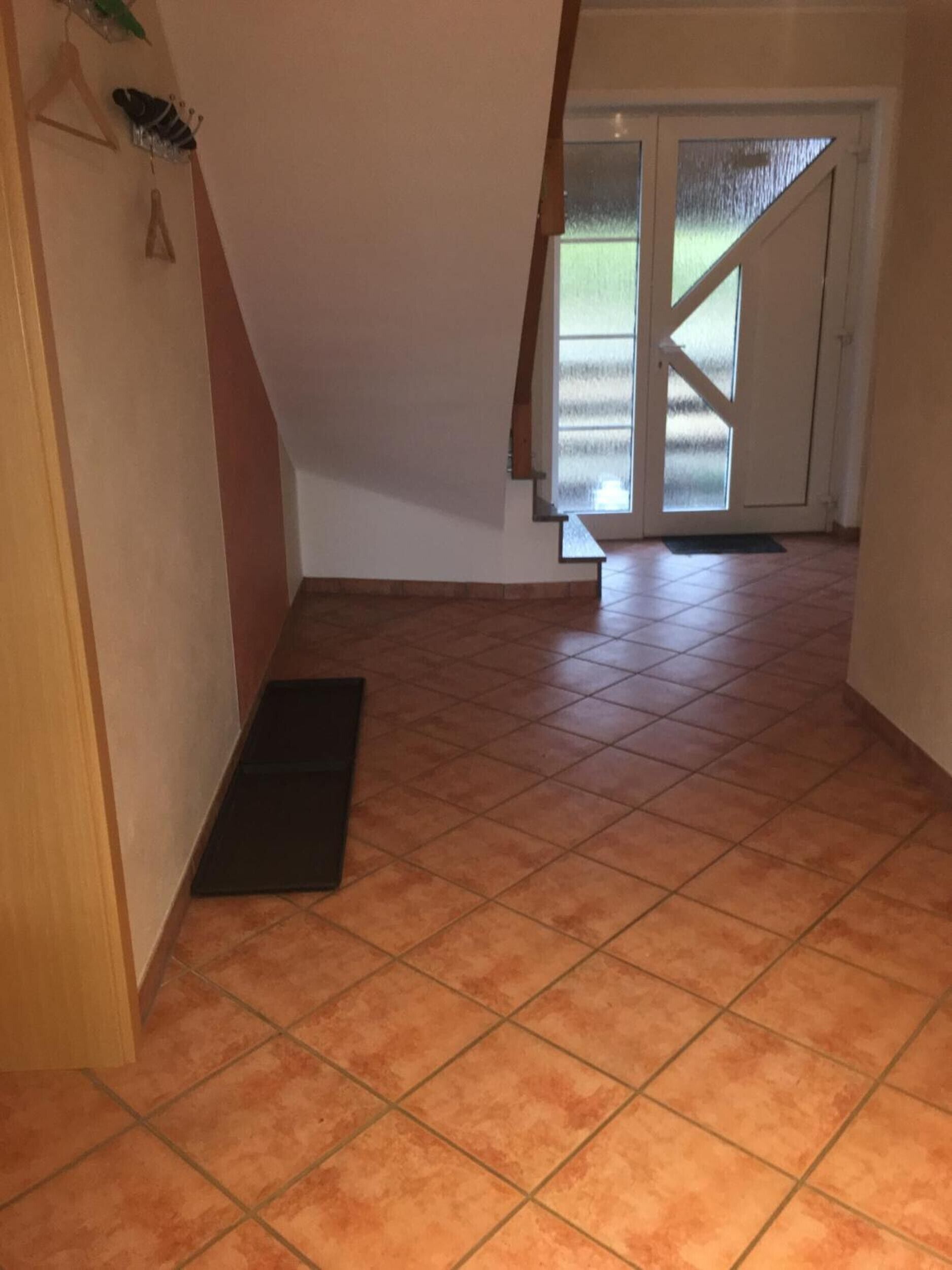 Un pasillo con piso de baldosas, una puerta de madera y una puerta de vidrio que da al exterior.