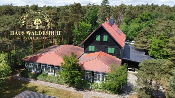 A large, two-story building with a red roof, surrounded by dense forest.