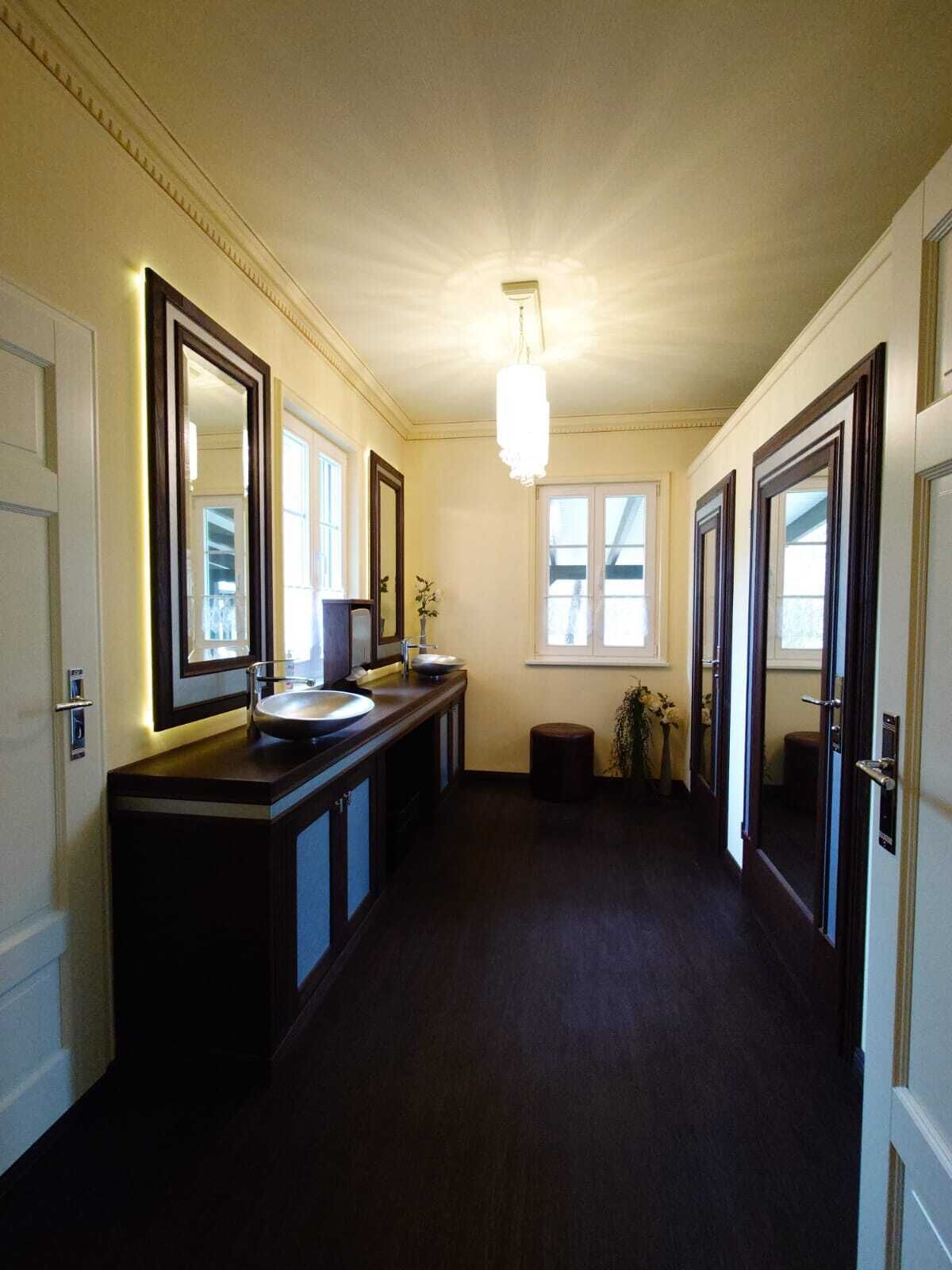 A long, narrow hallway with a dark wooden floor, a large mirror on the left, and a light fixture on the ceiling.