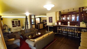 A cozy living room with a sofa, armchairs, and a coffee table. There is a bar area with stools and a counter.
