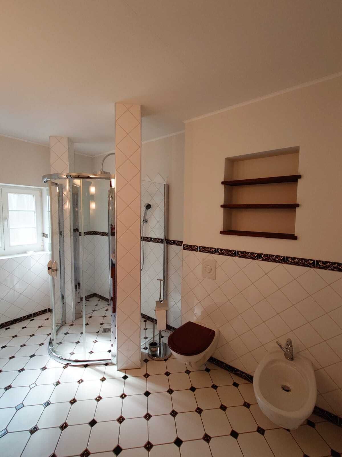 A bathroom with a glass shower enclosure, a white sink, and a red bath seat.