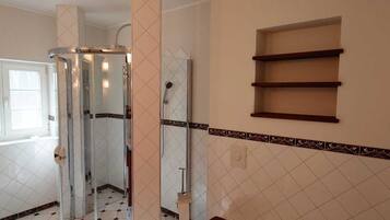 A bathroom with a glass shower enclosure, a white sink, and a red bath seat.