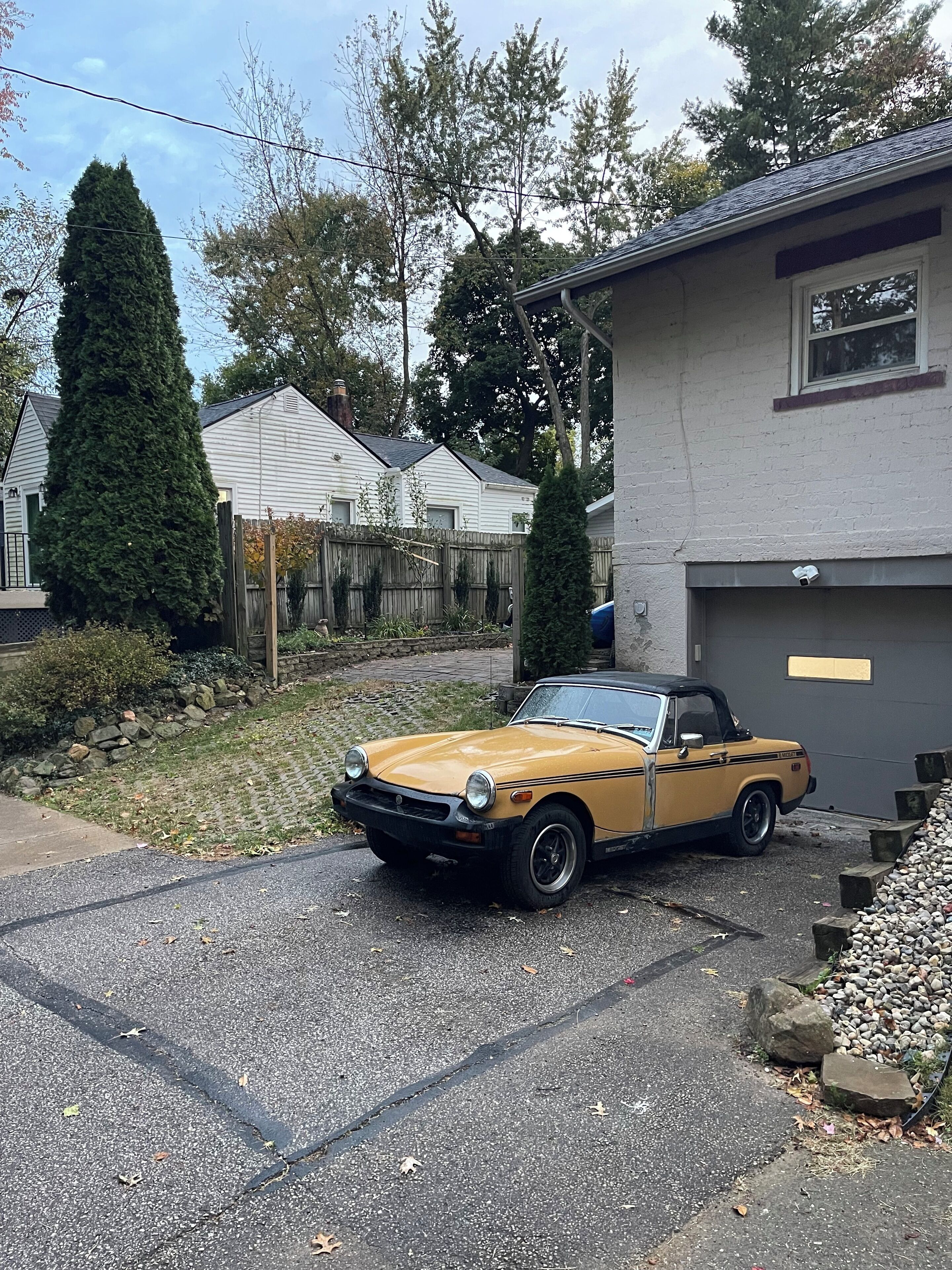 Une voiture décapotable jaune est garée dans une allée, avec une maison en arrière-plan.